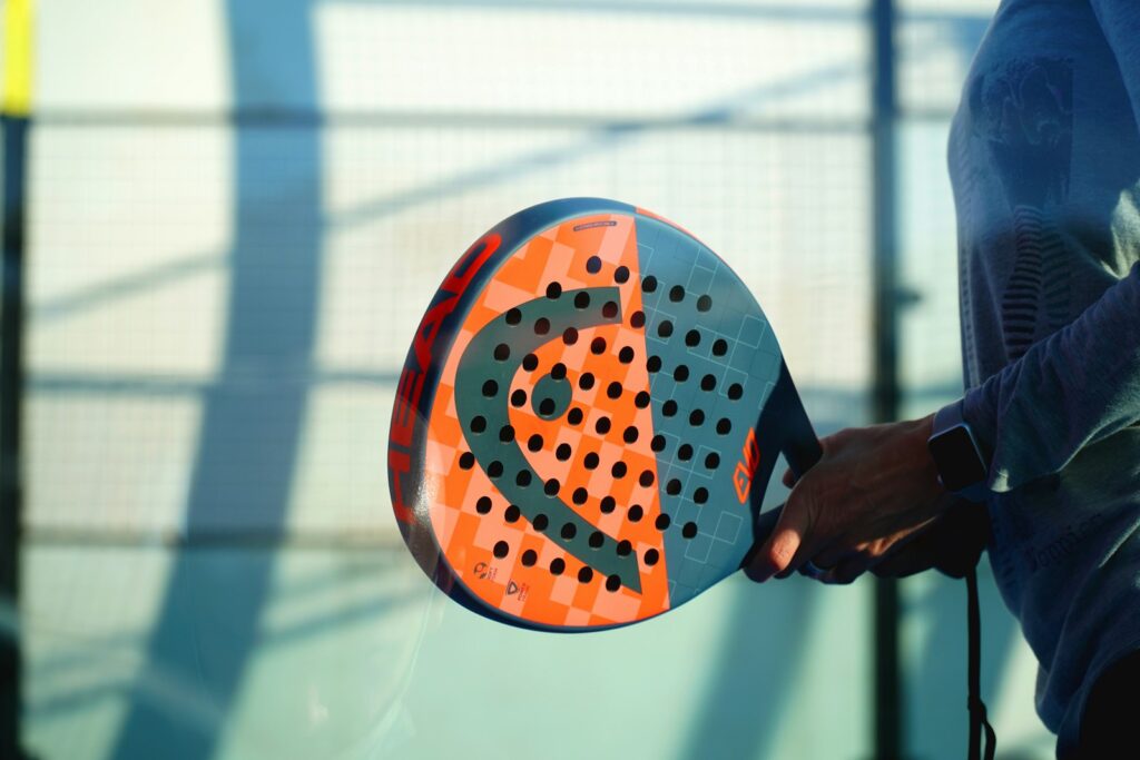 Spelare håller ett orange och blått padelrack