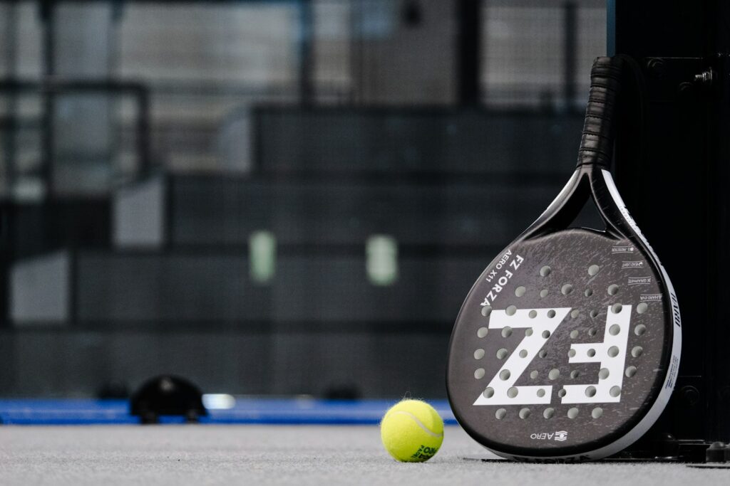Padelrack och gul boll på en grå bana